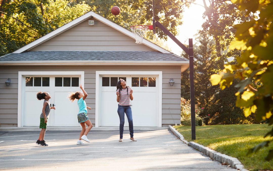 Mother And Children Playing Basketball On Driveway At Home